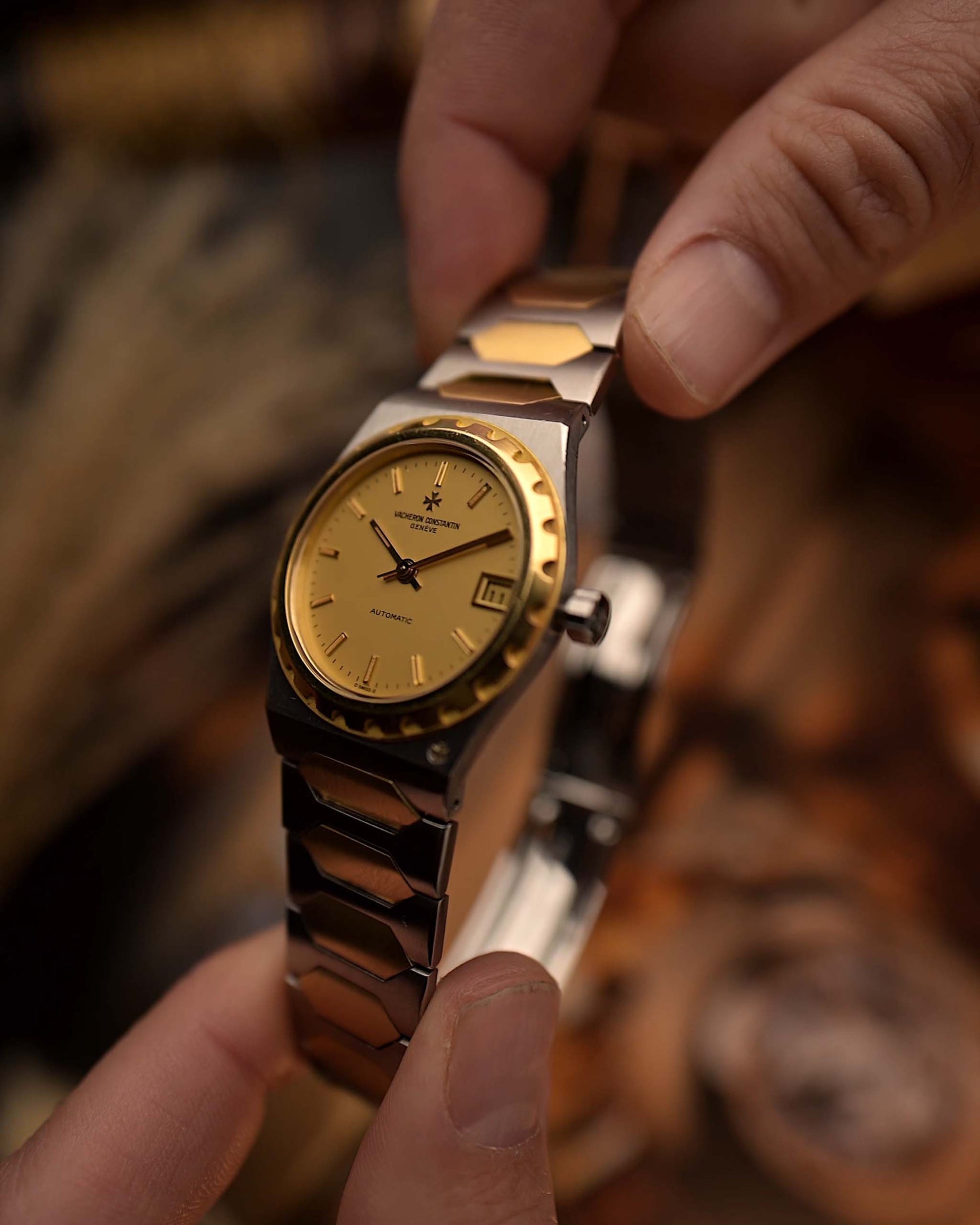 Close-up of a person holding a Vacheron Constantin 222 Ref 46003 Vintage watch from the 1980s, two-tone steel and 18k gold, golden Sigma dial, on a wrist on blurred background
