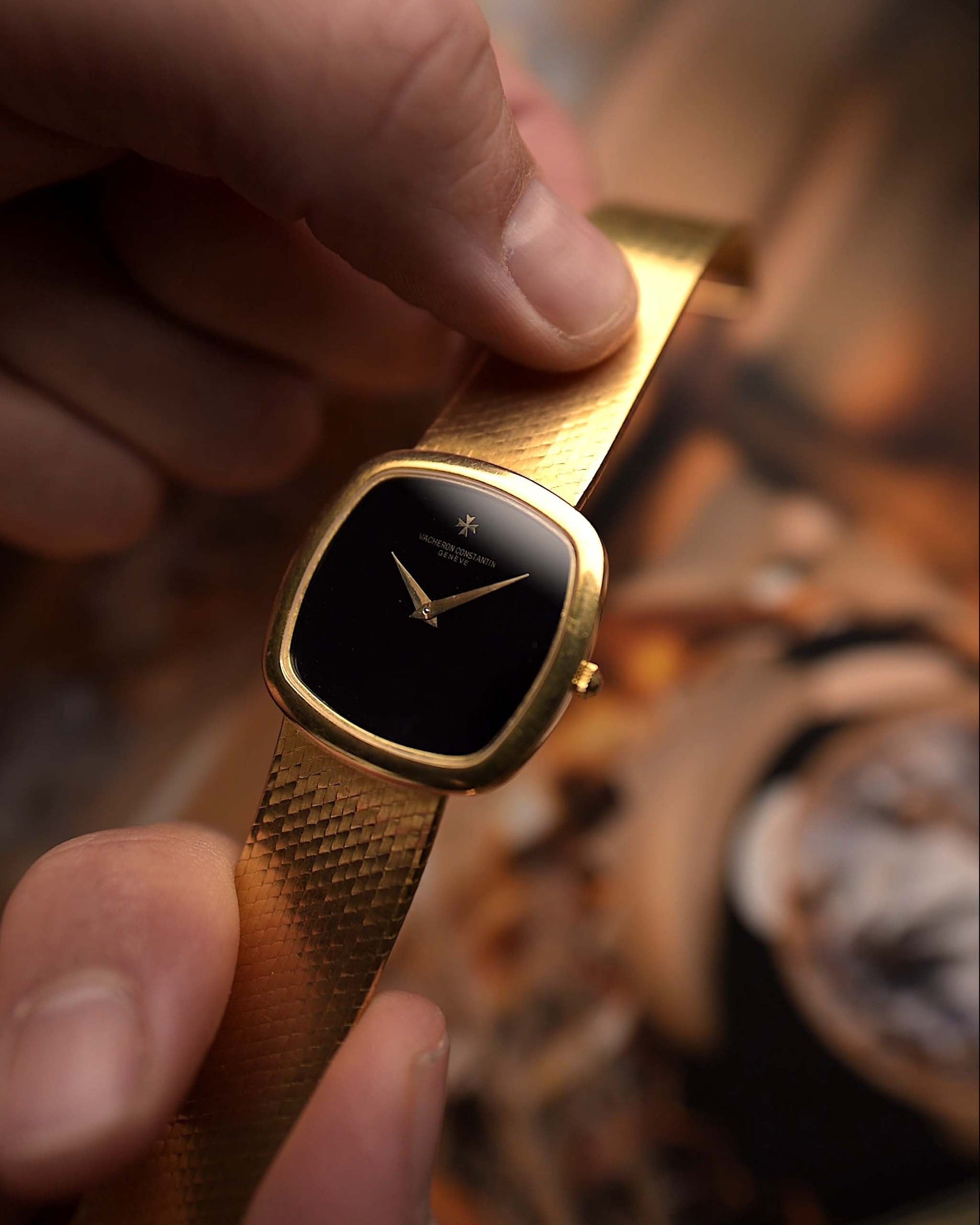 Vacheron Constantin 2099 Cushion Vintage watch from the 1970s, 18k yellow gold, Onyx dial, held by a hand against a blurred background