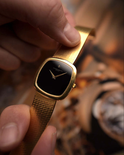 Vacheron Constantin 2099 Cushion Vintage watch from the 1970s, 18k yellow gold, Onyx dial, held by a hand against a blurred background